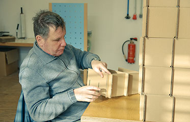 Vergrößerungsansichten für Bild: Ein Mann beim Zusammenbauen eines Holzkastens.